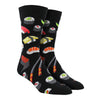 Shown on a foot form, a pair of Socksmith's black cotton men's crew socks with various types of sushi rolls and chopsticks in an all-over pattern