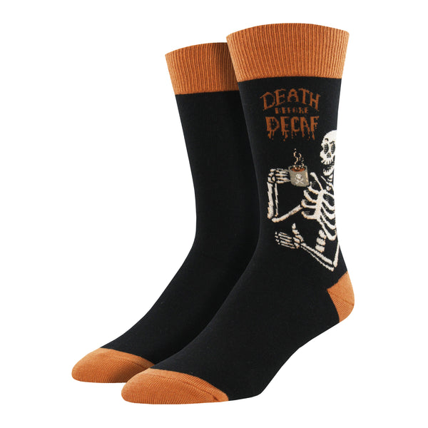 Shown on a foot form, a pair of Socksmith's black cotton men's crew socks with brown cuff/heel/toe and a skeleton drinking coffee along with the words “Death Before Decaf”
