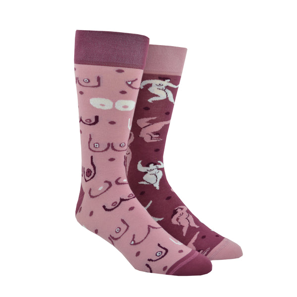 Shown in a size large on leg forms, a pair of mismatched Many Mornings brand unisex cotton crew socks. One sock has a dark pink heel/cuff/toe with a light pink base and cartoon images of different breast shapes. The second sock has light pink heel/cuff/toe and a darker pink base features an all over design of curvaceous nude feminine bodies.