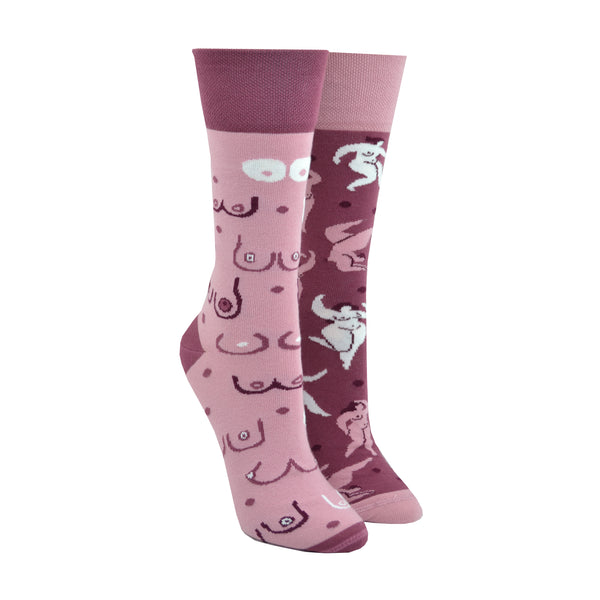Shown in a size small on leg forms, a pair of mismatched Many Mornings brand unisex cotton crew socks. One sock has a dark pink heel/cuff/toe with a light pink base and cartoon images of different breast shapes. The second sock has light pink heel/cuff/toe and a darker pink base features an all over design of curvaceous nude feminine bodies.