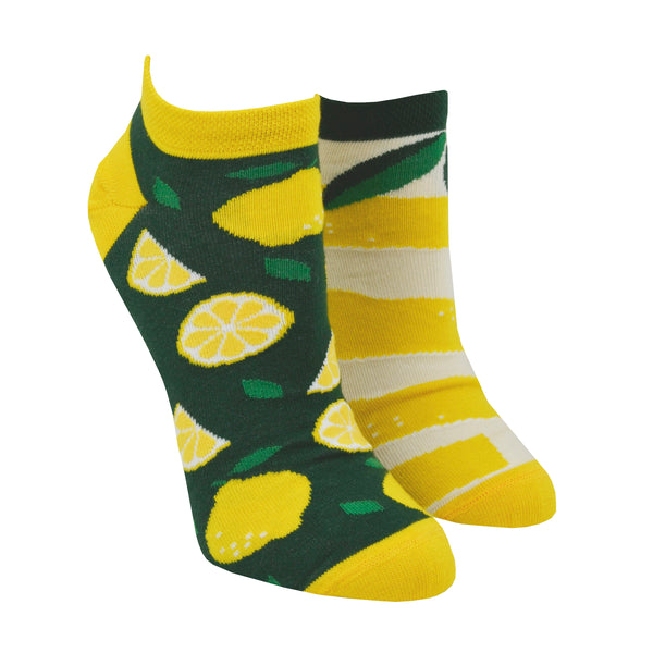 On a mannequin foot form, a pair of mismatched Many Mornings cotton socks are shown with one sock featuring whole and cut lemons while the other sock features a different lemon peel design.