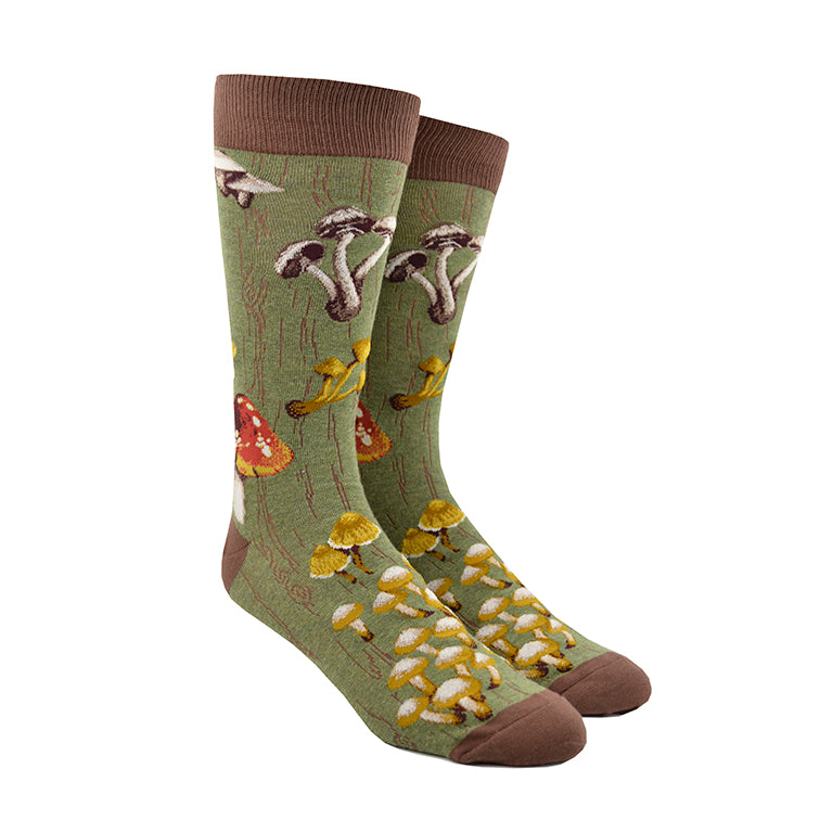 Shown on a foot form, a pair of Mod Socks’ green cotton men's crew socks with a large design of different kinds of mushrooms