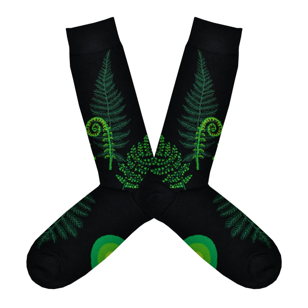 Shown in a flatlay, a pair of Mod Socks’ black cotton men's crew socks with green ferns and fiddleheads