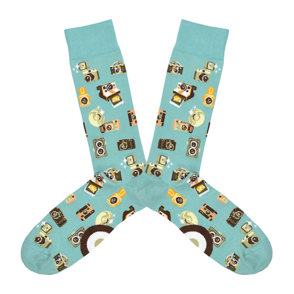 Shown in a flatlay, a pair of Mod Socks’ pale blue cotton men's crew socks with all-over pattern of various camera models