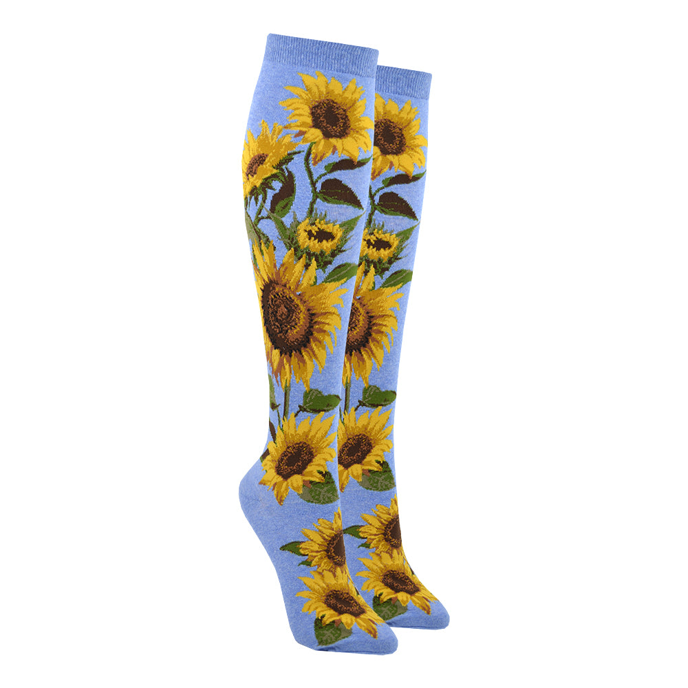 Shown on leg forms, a pair of sky blue knee high socks with realistic sunflowers going from the foot to the top of the sock.