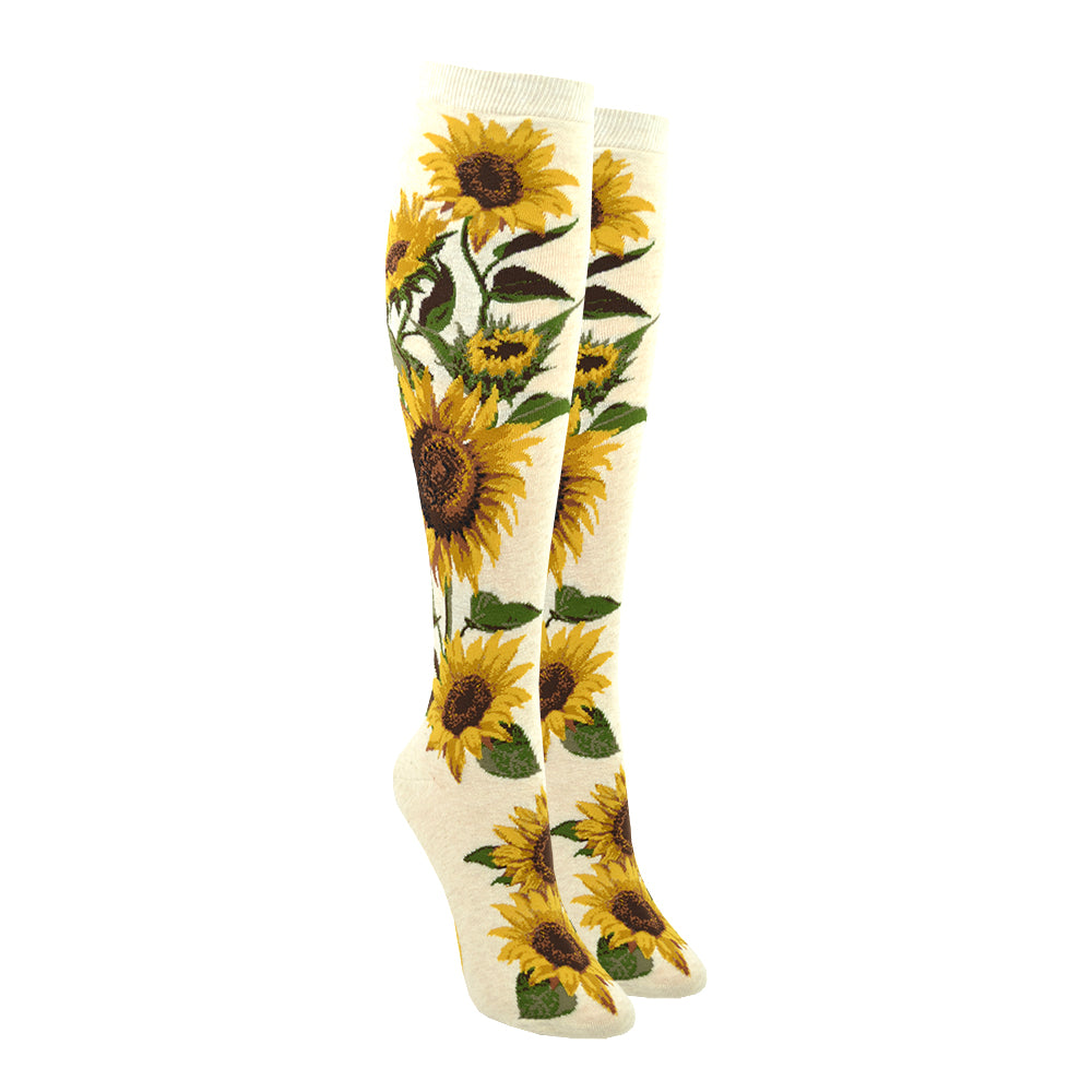 Shown on leg forms, a pair of cream colored knee high socks with realistic sunflowers climbing from the foot to the top of the sock. 
