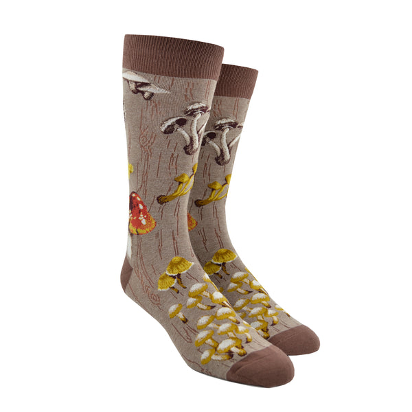 Shown on a foot form, a pair of Mod Socks’ brown cotton men's crew socks with a large design of different kinds of mushrooms