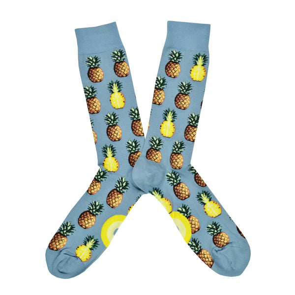 Shown in a flatlay, a pair of Mod Socks’ pale blue cotton men's crew socks with whole or halved pineapples