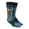 Shown on a leg form, these heathered blue/green and black funny men's cotton crew socks by Mod Socks feature Big Foot walking amongst the trees drinking a beer.