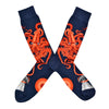 Shown in a flatlay, a pair of Mod Socks’ dark blue cotton men's crew socks with large orange squid catching the tail of a gray whale