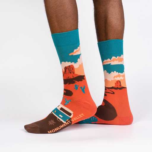 A pair of cotton Sock it to Me socks shown on a persons feet featuring a scene from Monument Valley National Park
