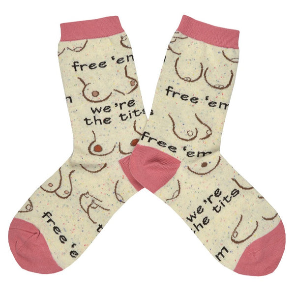 Shown in a flatlay, a pair of Oooh Yeah women's cotton crew socks in light tan with a pink heel, toe, and cuff. These socks feature various breast designs and shapes with the text "Free 'Em! We're the Tits!".