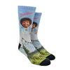 Shown on a leg form, a pair of Oooh Yeah’s cotton men’s crew socks with light blue nature-scape and Bob Ross portrait