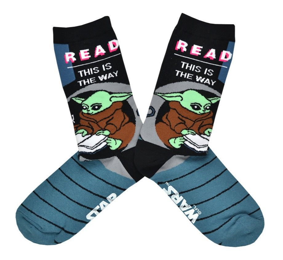 These blue and black cotton unisex crew socks by the brand Out of Print feature the Star Wars Mandalorian character Baby Yoda reading, with the text 