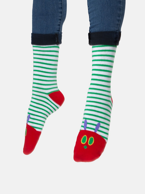 Shown on a model with feet relaxed, a pair of green and white striped cotton Out of Print brand unisex crew socks. These socks feature a red heel and toe with the iconic Very Hunger Caterpillar face on the toe.