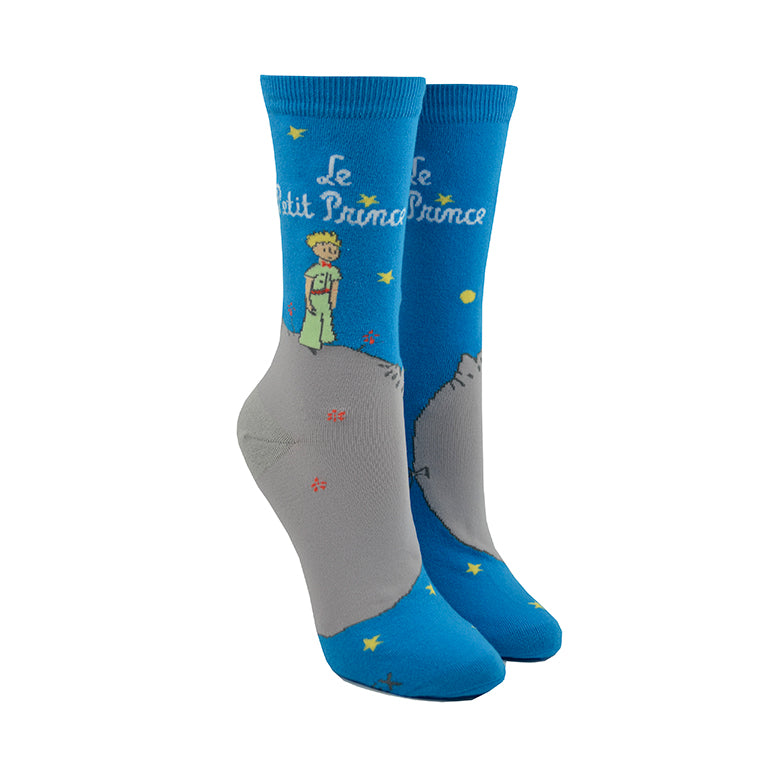 Shown on leg forms, a pair of Out of Print brand unisex cotton crew socks in blue and grey. These socks feature a little cartoon boy outside at night with the words, 