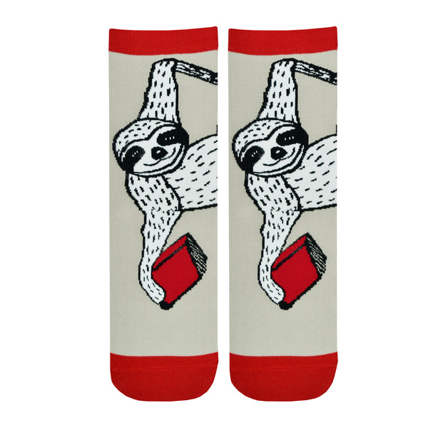 Shown in a flatlay, a pair of Out of Print brand unisex cotton crew socks in tan with a red heel/toe/cuff and a black sole. The sock features a black and white cartoon sloth hanging from a vine with a red book.