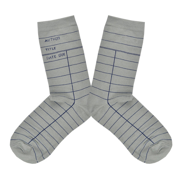 These gray cotton unisex crew socks by the brand Out of Print feature the iconic library card design with the words "Author, Title, Date Due" written on the leg and a grid for filling in the information running down the leg and foot.