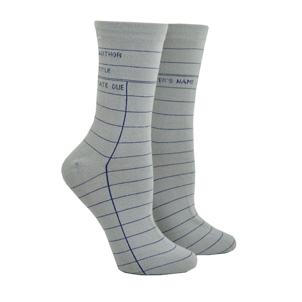 Shown on a leg form in the women's size, these gray cotton unisex crew socks by the brand Out of Print feature the iconic library card design with the words "Author, Title, Date Due" written on the leg and a grid for filling in the information running down the leg and foot.