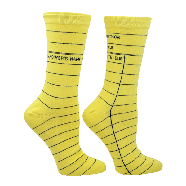 A side view shown on a leg form in the women's size, these yellow cotton unisex crew socks by the brand Out of Print feature the iconic library card design with the words "Author, Title, Date Due" written on the leg and a grid for filling in the information running down the leg and foot.