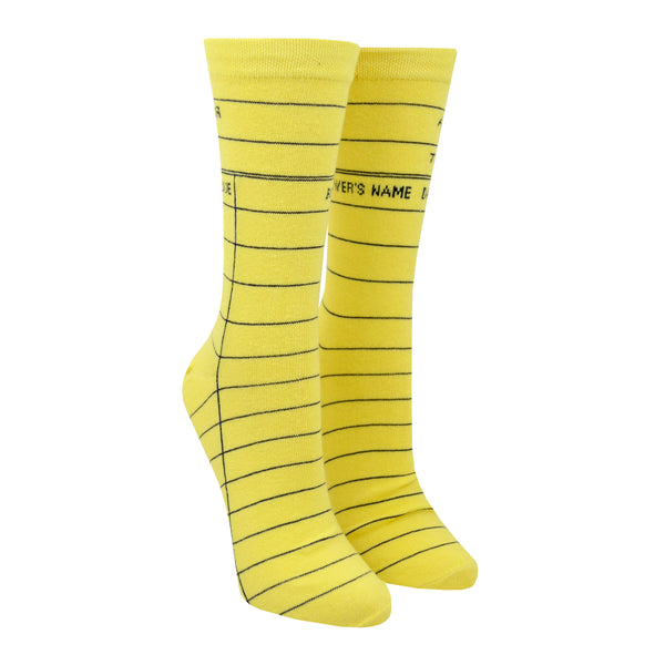 Shown on a leg form in the women's size, these yellow cotton unisex crew socks by the brand Out of Print feature the iconic library card design with the words "Author, Title, Date Due" written on the leg and a grid for filling in the information running down the leg and foot.