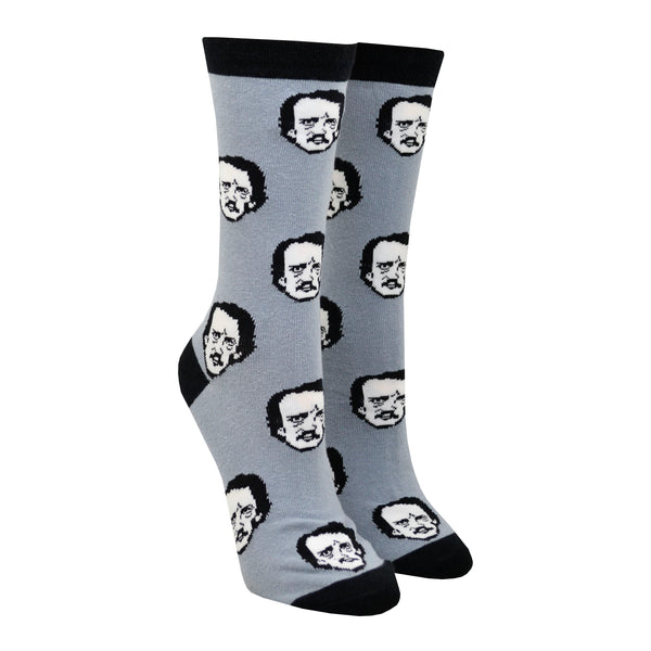 Shown on leg forms, a pair of Out of Print brand unisex cotton crew socks in grey with black heel/toe/cuff. The sock features all over motif of cartoon Edgar Allen Poe faces as if they were polka-dots.