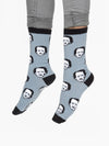 Shown on a models feet, a pair of Out of Print brand unisex cotton crew socks in grey with black heel/toe/cuff. The sock features all over motif of cartoon Edgar Allen Poe faces as if they were polka-dots.