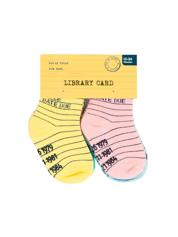 Shown in the packaging, this 4 pack of kid's cotton crew socks in yellow, pink, blue and green by the brand Out of Print feature the iconic library card design with the words "Author, Title, Date Due" written on the leg and a grid for filling in the information running down the leg and foot.