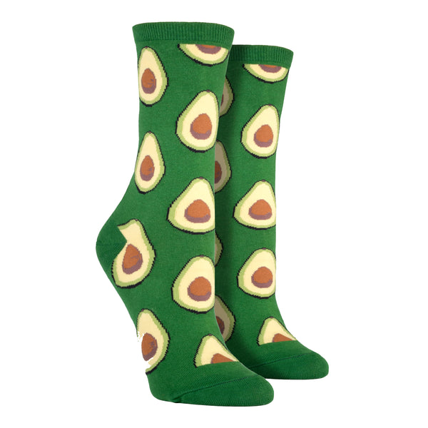 Shown on a leg form, these green cotton women's novelty crew socks by the brand Socksmith feature light green avocados sliced in half showing their brown pits.