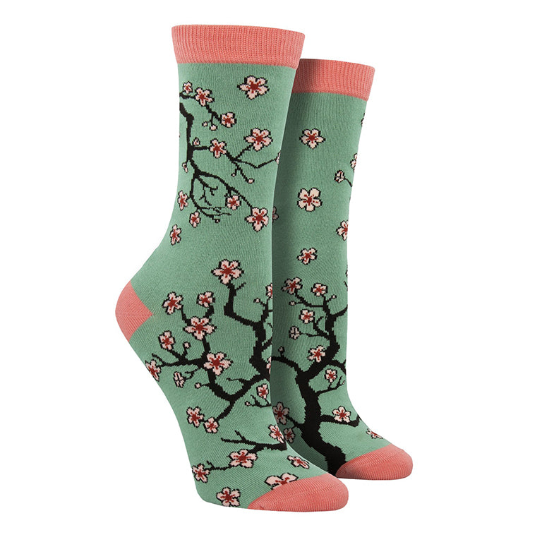 Shown on leg forms, a pair of Socksmith brand women's bamboo crew socks in sage green with a pink heel, toe, and cuff. This sock features an all over design cherry blossom branches reaching around the sock.
