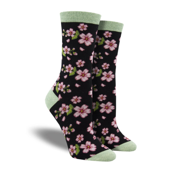 Shown on leg forms, a pair of Socksmith brand women's bamboo crew socks in black with a sage green toe, heel, and cuff. This sock features a pink and white flower design with green accents all over the sock.