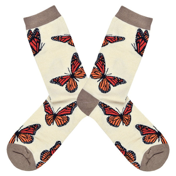 Shown in a flatlay, a pair of Socksmith brand women's bamboo crew socks in ivory with a heather brown toe, heel, and cuff. This sock features red, orange, and black monarch butterflies all over.