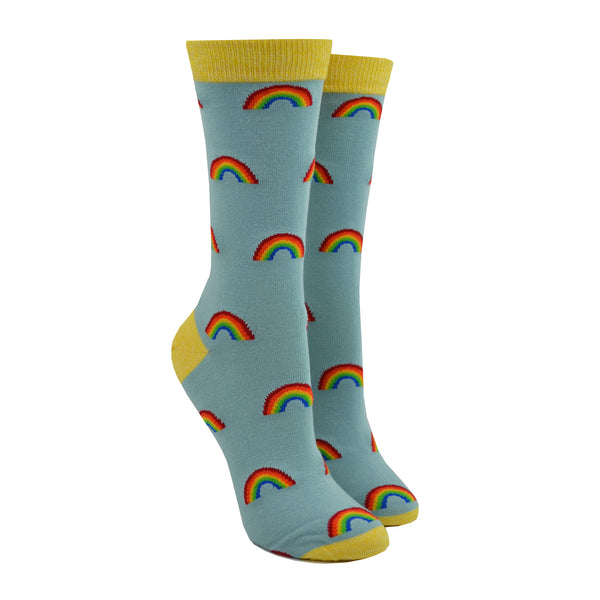 Shown on leg forms, a pair of Socksmith brand women's bamboo crew socks in light blue with a yellow toe, heel, and cuff. This sock has an all over motif of little rainbows.
