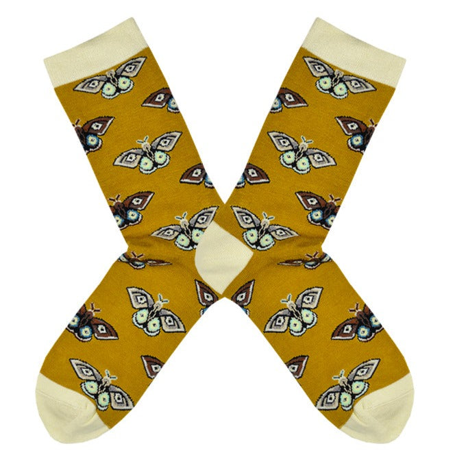 Shown in a flatlay, a pair of Socksmith brand women's bamboo crew socks in gold with an ivory heel, toe, and cuff. This sock has an all over motif of vintage Polyphemus moths in brown, blue, black, and white.