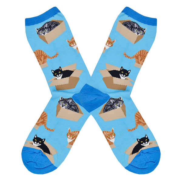 Shown in a flatlay, a pair of Socksmith’s blue cotton women’s crew socks with various cats sitting in cardboard boxes