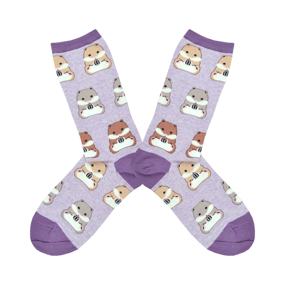 Shown in a flatlay, a pair of women's Socksmith brand cotton and nylon crew sock in lilac with a purple heel, toe, and cuff. These socks feature an all over pattern of grey, blonde, and brown hamsters holding a little sunflower seed.