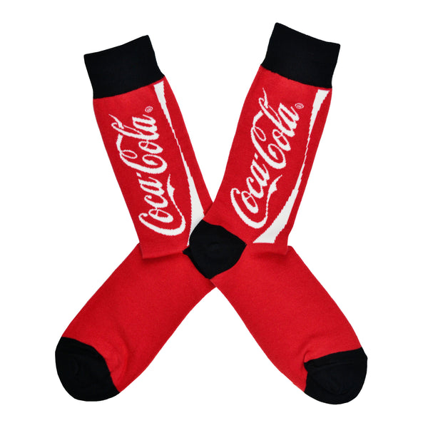 Shown in a flatlay, a pair of Socksmith's red cotton men's crew socks with Coca-Cola logo text and black cuff/heel/toe