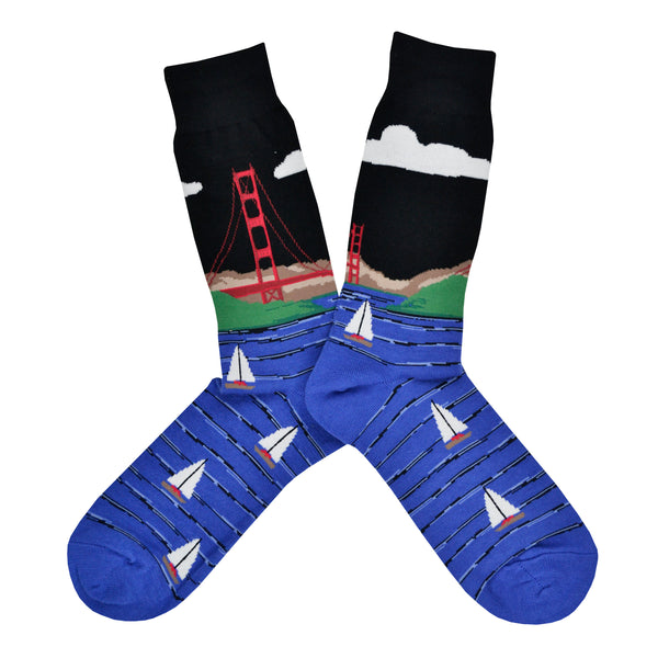 These black cotton men's crew socks by the brand Socksmtih feature the iconic landmark of San Francisco, the Golden Gate Bridge, towering above the beautiful blue San Francisco Bay filled with sailboats.