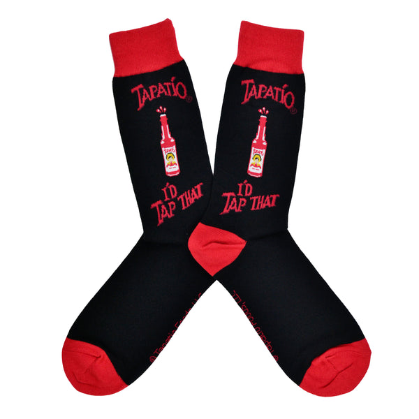 Shown in a flatlay, a pair of Socksmith's black cotton men's crew socks with red cuff/heel/toe, Tapatio hot sauce bottle and the text “Tapatio: I’d Tap That!”