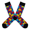 Shown in a flatlay, a pair of Socksmith's cotton men's crew socks with black cuff/heel/toe and large all-over pattern of puzzle pieces in blue, red and yellow