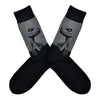 Shown in a flatlay, a pair of Socksmith's black cotton men's crew socks with gray raptor dinosaur head design