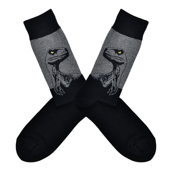 Shown in a flatlay, a pair of Socksmith's black cotton men's crew socks with gray raptor dinosaur head design