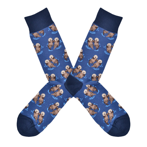 These blue cotton men's crew socks with a navy heel, toe and cuff by the brand Socksmith feature adorable otters floating in the ocean holding hands.