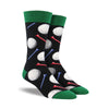 Shown on a foot form, a pair of Socksmith's black cotton men's crew socks with dark green cuff/heel/toe and all-over pattern of golf balls and tees