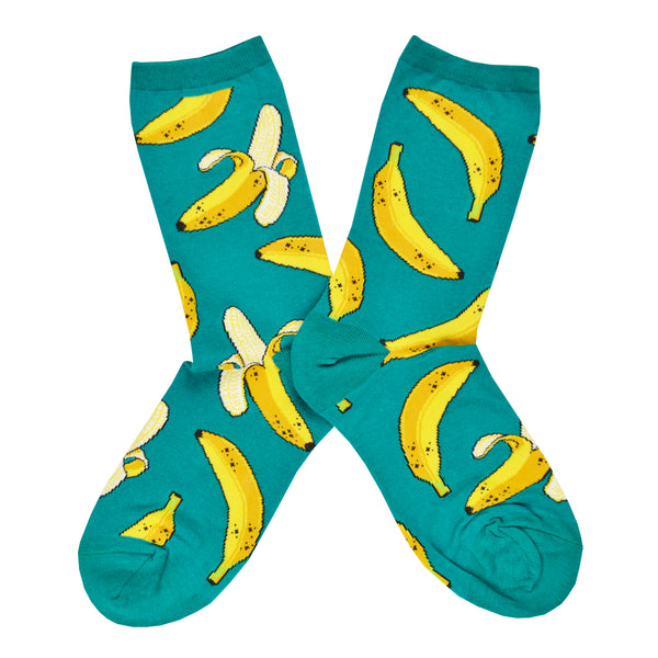Shown in a flatlay, a pair of Socksmith's teal-green cotton women’s crew socks with ripe green banana fruit pattern