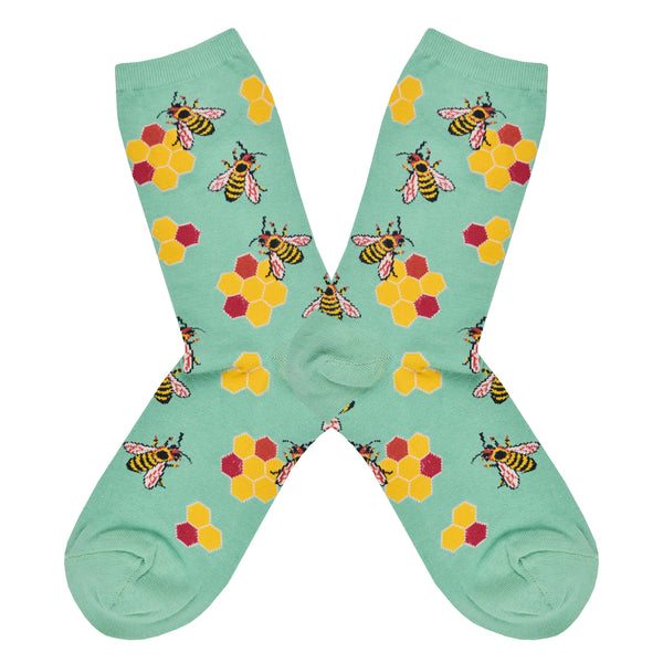 Shown in a flatlay, a pair of Socksmith’s light green cotton women’s crew socks with bee print including yellow honeycombs