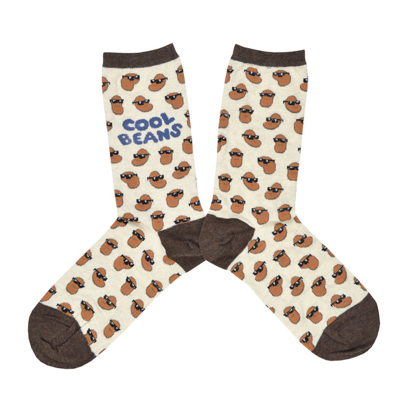 Shown in a flatlay, a pair of Sock Smith brand women's cotton crew socks in ivory with a brown heel, toe, and cuff. The sock features an all over motif of little brown beans in black sunglasses, the leg of the sock reads, "Cool Beans" in a blue font.