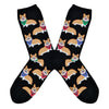 Shown in a flatlay, a pair of Sock Smith brand women's cotton crew socks in black featuring an all over motif of blonde corgis in blue, red, and green bandanas.