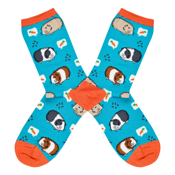Shown in a flatlay, a pair of women's Socksmith brand cotton crew socks in teal with an orange heel, toe, and cuff. The sock has an all over design of guinea pigs thinking about carrots.