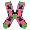 Shown in a flat lay, a pair of women's fit Sock Smith cotton crew socks in pink with a green heel, toe, and cuff. These socks have realistic black labs all over the sock. 